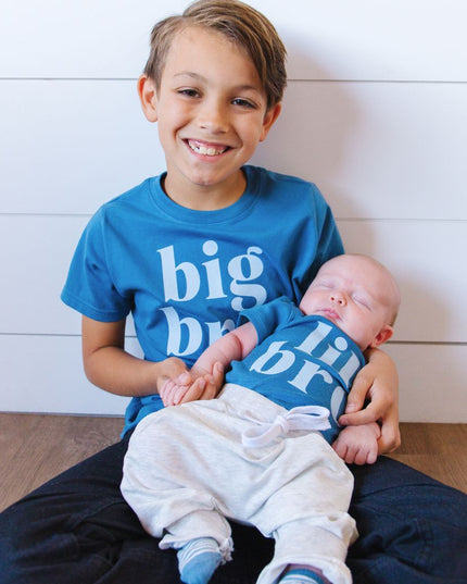 Boy holding baby wearing matching big bro/lil bro blue shirts