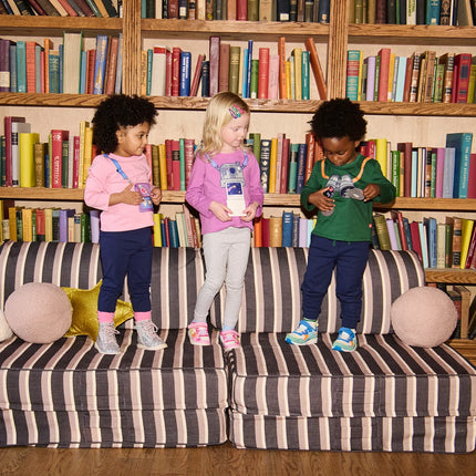 Three children standing on a striped sofa in front of a bookshelf 