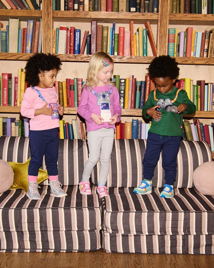 Three children standing on a striped sofa in front of a bookshelf 
