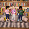 Three children standing on a striped sofa in front of a bookshelf 