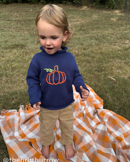 A boy standing wearing a blue rollneck sweater with a pumpkin design 