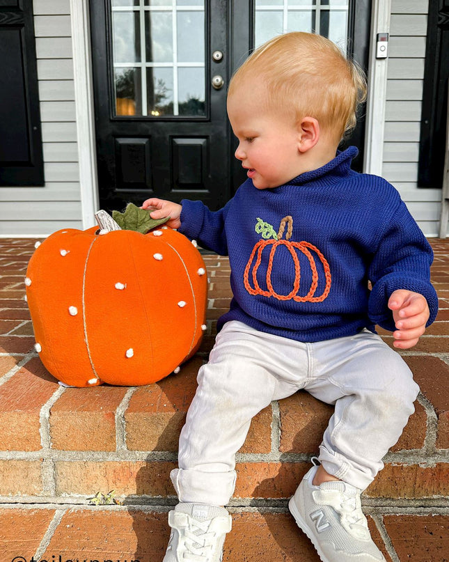 Baby sitting wearing a blue rollneck sweater with a pumpkin design 