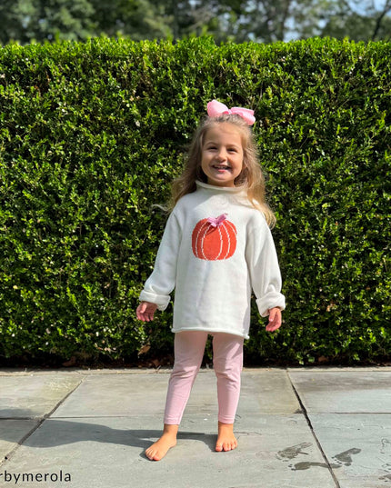 Young girl wearing rollneck sweater with a pumpkin design and pink bow 