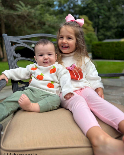Two children sitting wearing pumpkin sweaters 
