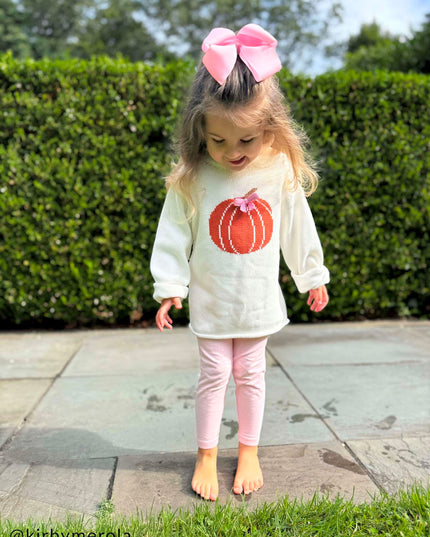 Young girl wearing rollneck sweater with a pumpkin design and pink bow 
