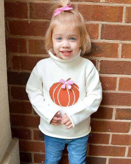 Young girl wearing rollneck sweater with a pumpkin design and pink bow 