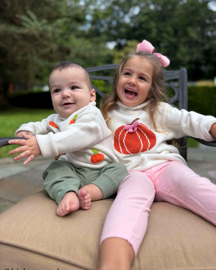two kids sitting wearing pumpkin sweaters