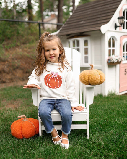 Young girl wearing rollneck sweater with a pumpkin design and pink bow 