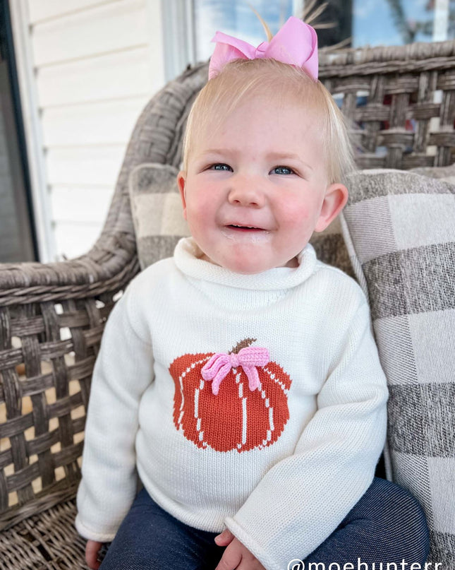 Baby wearing rollneck sweater with a pumpkin design and pink bow 