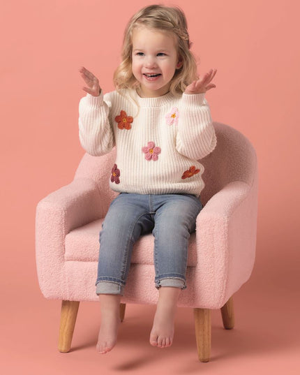 Girl sitting wearing cream sweater with crochet flowers and jeans