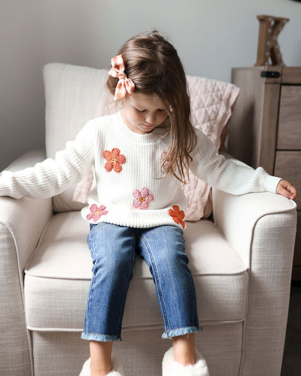Girl wearing cream sweater with crochet flowers and jeans