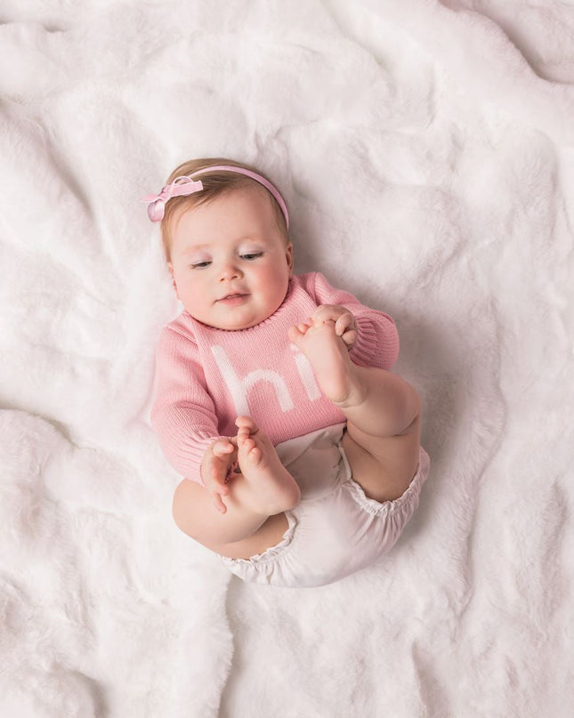 Baby wearing a pink sweater with 'hi' printed on it