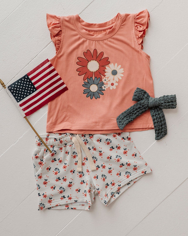 Orange shirt with red, white and blue flowers paired with white shorts with red and blue floral print 