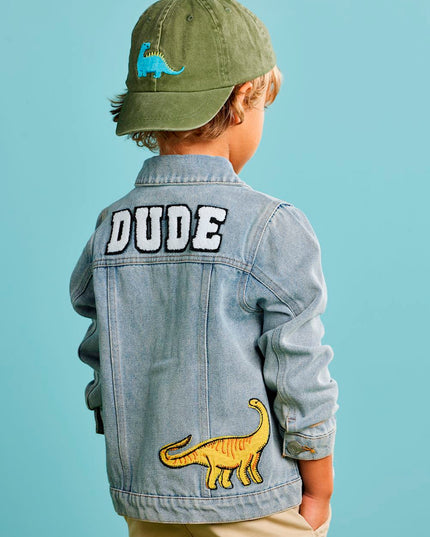 Child wearing a denim jacket with dude and dinosaur patches
