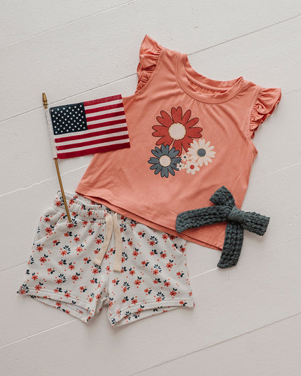 Orange shirt with red, white and blue flowers paired with white shorts with red and blue floral print 
