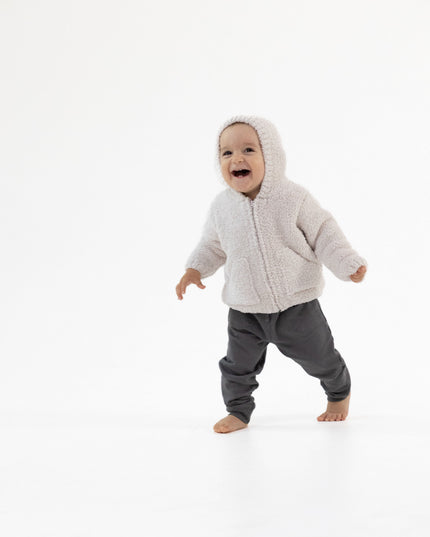 A baby wearing a light beige chenille hooded zip-up jacket and dark gray pants.