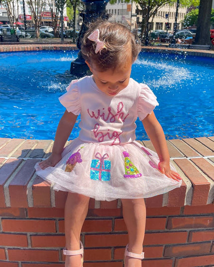 Child wearing 'Wish big' t-shirt sitting by a fountain