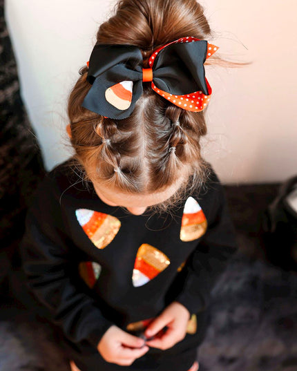 Girl wearing Black sweatshirt with sequin candy corn patches and orange striped leggings 