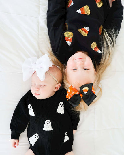 Girl wearing Black sweatshirt with sequin candy corn patches and orange striped leggings laying with baby wearing ghost romper