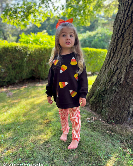 Girl wearing Black sweatshirt with sequin candy corn patches and orange striped leggings 