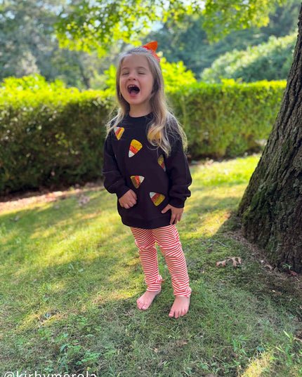 Girl wearing Black sweatshirt with sequin candy corn patches and orange striped leggings 