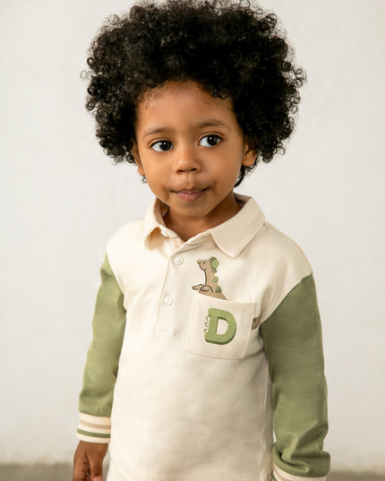 Boy wearing children's long sleeve polo shirt with green sleeves and a pocket featuring a dinosaur peeking out