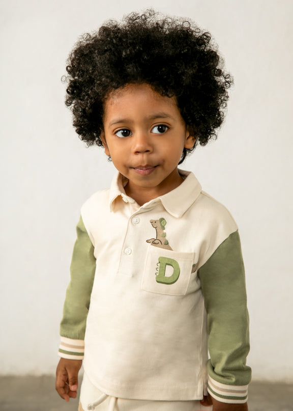 Boy wearing children's long sleeve polo shirt with green sleeves and a pocket featuring a dinosaur peeking out