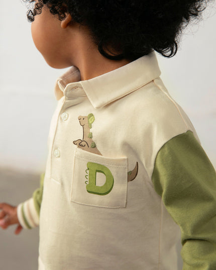 Boy wearing children's long sleeve polo shirt with green sleeves and a pocket featuring a dinosaur peeking out