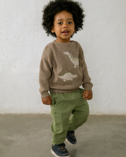 Child wearing a brown sweater with dinosaur design and green pants
