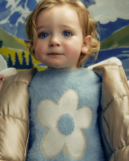 A little girl wearing A light blue fuzzy long-sleeve sweater with a large cream-colored flower