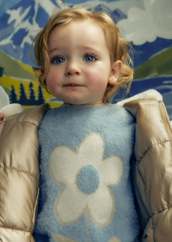 A little girl wearing A light blue fuzzy long-sleeve sweater with a large cream-colored flower
