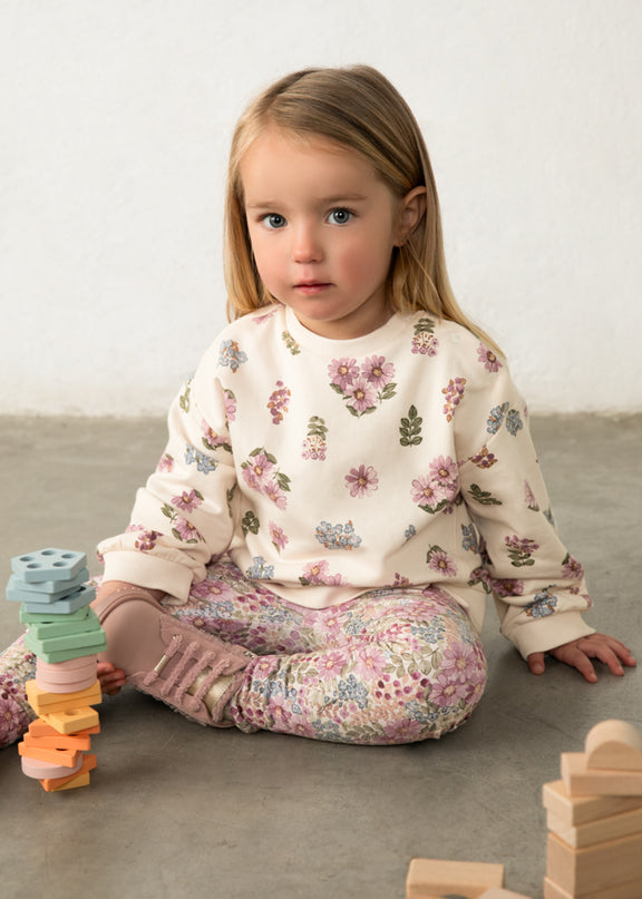 Girl wearing cream colored sweatshirt with purple, blue and green floral print and floral printed pants
