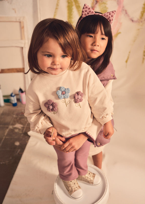 Girl wearing Cream colored sweatshirt with crocheted flowers and mauve pants