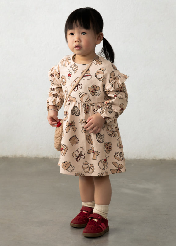 Girl wearing Cream colored dress with pastry print and croissant purse