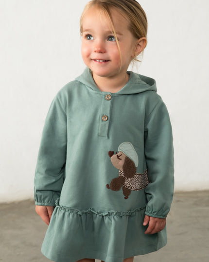 Girl wearing green hooded dress with a brown and white spotted dog appliqué 
