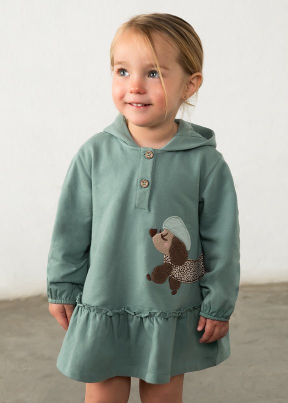 Girl wearing green hooded dress with a brown and white spotted dog appliqué 