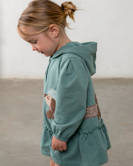 Girl wearing green hooded dress with a brown and white spotted dog appliqué 