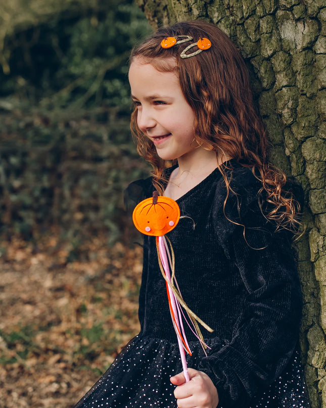 A girl holding a whimsical smiling pumpkin wand with colorful ribbon streamers