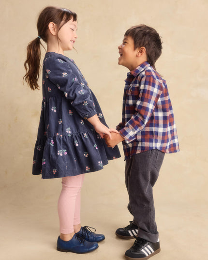 a young girl wearing a deep midnight corduroy shirtdress with floral pattern and pink leggings and a boy wearing a plaid shirt and black jeans