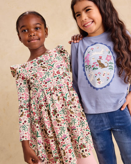 A young girl wearing a floral dress and another girl wearing a long sleeve blue graphic tee and blue velour pants
