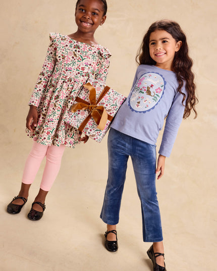 A young girl wearing a floral dress and another girl wearing a long sleeve blue graphic tee and blue velour pants