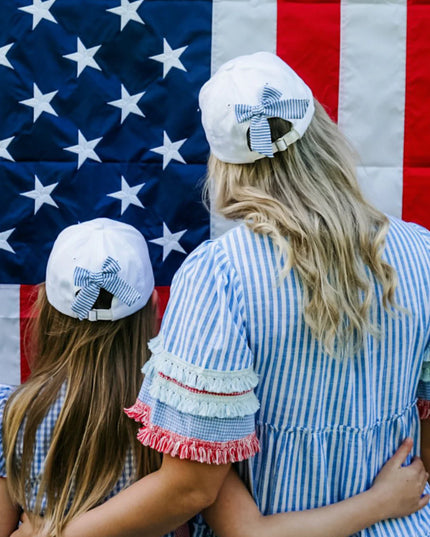 Woman and girl wearing matching baseball hats with blue and white bows