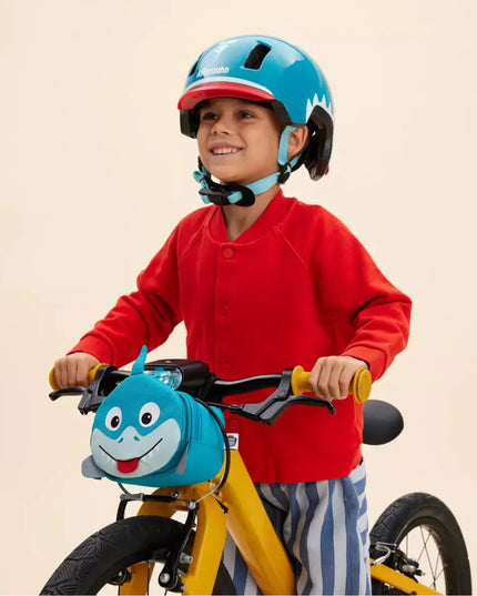 Child  riding a yellow bicycle with a blue shark handlebar bag