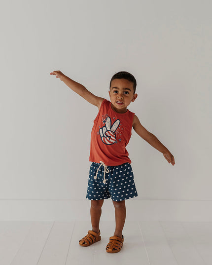 Boy wearing  red tank top with peace sign design and navy shorts with white stars. 