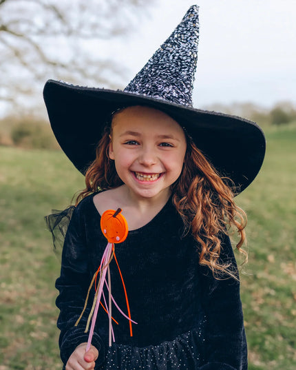 A girl dressed as a witch  holding a whimsical smiling pumpkin wand with colorful ribbon streamers