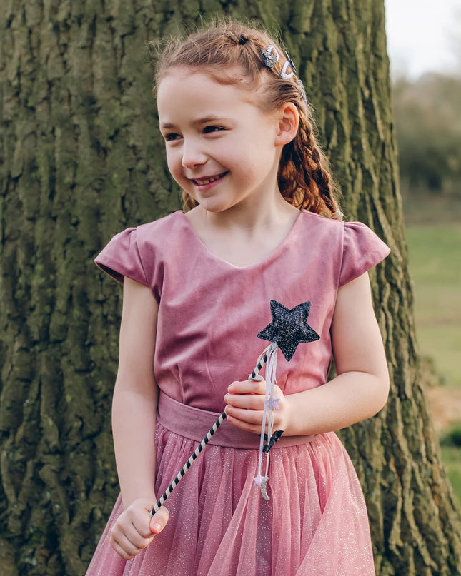 A girl holding a Halloween-themed wand with a black glittery star top, a black-and-white striped wand handle, and dangling ribbons featuring small bat, star and moon shapes. 