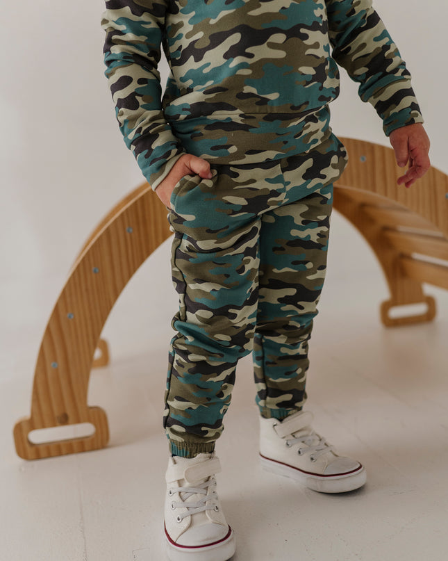 A child wearing a matching camouflage sweatshirt and jogger pants set with white sneakers