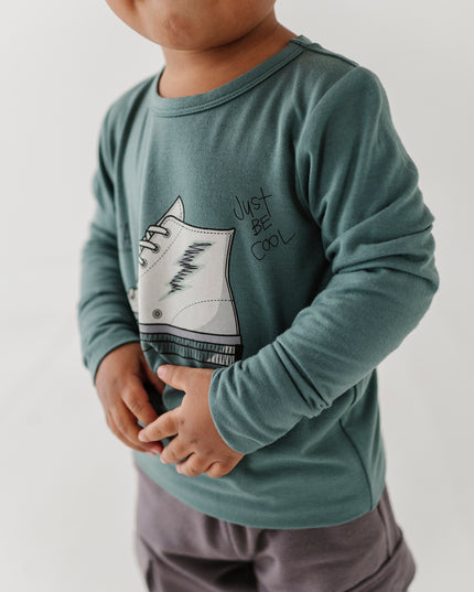 Boy wearing green long sleeve tee with sneaker design and grey pants