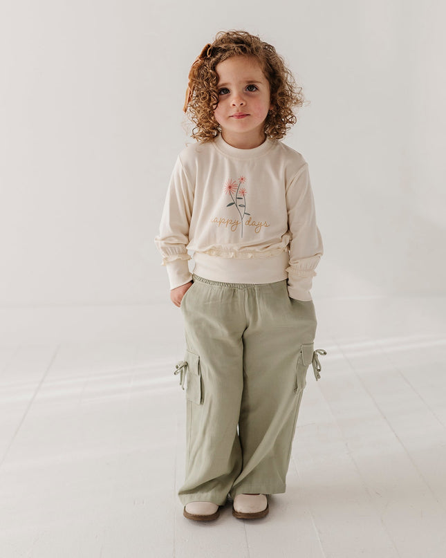 Girl wearing cream color sweatshirt with floral 'happy days' design and green cargo pants