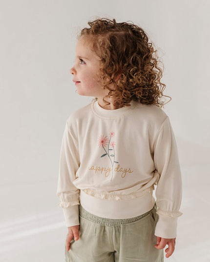 Girl wearing cream color sweatshirt with floral 'happy days' design and green cargo pants